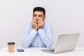 Scared nervous man employee sitting in office workplace with laptop and coffee, biting nails, panicking terrified of troubles