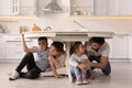 Scared parents with their children hiding under table in kitchen during earthquake Royalty Free Stock Photo