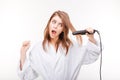 Scared pretty young woman in bathrobe using hair straightener