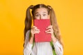 Scared School Girl Hiding Face Behind Book, Yellow Background Royalty Free Stock Photo