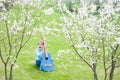 Scared screaming cute little girl with guitar sitting on green grass under blooming trees in spring park