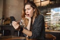 Scared shocked displeased beautiful young pretty woman sitting in cafe indoors using mobile phone talking with friends Royalty Free Stock Photo