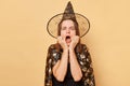 Scared shocked frighten woman wearing witch costume and cone hat isolated over beige background screaming with eyes full of fear