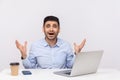 Scared shocked man employee sitting in office workplace with laptop and coffee, raising hands, looking big eyes