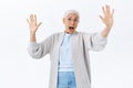 Scared and shocked old lady being frightened by grandchild jumping from corner, raising hands in surrender and fear