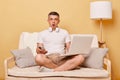 Scared shocked surprised man wearing white T-shirt and shorts sitting on sofa against beige background looking at camera with big Royalty Free Stock Photo