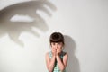 Scared small girl wearing casual sleeveless t shirt being afraid of shadows of hands on wall, looking at camera with frightened Royalty Free Stock Photo