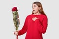 Scared surprised young European woman keeps hand on chest, looks with wonder at bouquet of red beautiful roses, wears casual