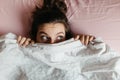 Scared and surprised young woman with open eyes hiding face under blanket, pretty frightened and curious girl feeling shy peeking Royalty Free Stock Photo