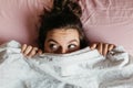Scared and surprised young woman with open eyes hiding face under blanket, pretty frightened and curious girl feeling shy peeking Royalty Free Stock Photo