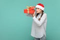 Scared teenager girl in Santa Claus hat, holding present box, looking inside with big eyes.