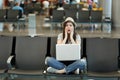 Scared traveler tourist woman with laptop sitting with crossed legs, clinging to face, waiting in lobby hall at airport