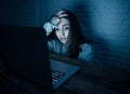 Scared woman on laptop in the dark feeling fear suffering online harassment and cyberbullying