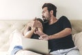 Scared young couple sitting under blanket on the bed with laptop while watching horror movie at tv together in the bedroom. Royalty Free Stock Photo