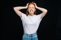 Scared young woman with closed eyes wearing T-shirt and denim pants screaming with hands on head