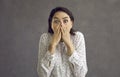 Scared young woman covering mouth with hand looking at camera studio shot