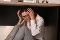 Scared young woman hiding under office desk during earthquake