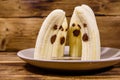 Scary banana ghosts in ceramic plate on a wooden table. Halloween concept