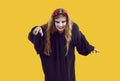 Woman trying to catch somebody in halloween costume with terrifying makeup on yellow background.