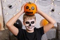 Scary child with a make-up in form of a skeleton and with a pumpkin in his hands