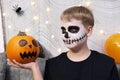 Scary child with a make-up in form of a skeleton and with a pumpkin in his hands