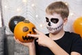 Scary child with a make-up in form of a skeleton and with a pumpkin in his hands