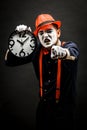 Scary clown pantomime with a clock in his hands, on a dark background Royalty Free Stock Photo