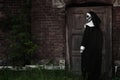 Scary devilish nun near wooden door outdoors, space for text. Halloween party look