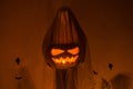 Scary ghost holding Jack o lantern in dark. Scary atmospheric halloween decorations and person dressed as ghost with glowing