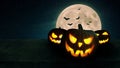 Scary glowing pumpkins with lights on a wooden table with a full moon and bats. Halloween wallpaper and background. Free space for Royalty Free Stock Photo