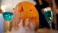 Scary Halloween pumpkin and smoky blue cocktails on party table, traditions