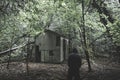 A scary hooded figure standing in a spooky forest next to an ruined hut. With a muted, eerie edit