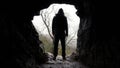 A scary horror figure, back to camera. Standing on the entrance to a cave. On a moody winters day in the countryside Royalty Free Stock Photo