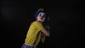 Scary juggler clown juggling axe in a dark room. Frightening jester, clown, buffoon.