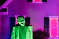 A scary life sized Frankenstein snimated monster glowing green against a purple lit house in October on Haloween