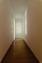 Scary light-walled hallway with a closed door illuminated by the dim shadow of a window, copy space Royalty Free Stock Photo