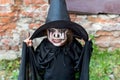 Scary little girl in a witch costume looking at camera with frightening expression on brick wall background. Halloween and day of