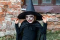 Scary little girl in a witch costume smiles on brick wall background. Happy Halloween. Halloween and day of the dead concept