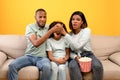 Scary moment in horror movie. African american parents closing daughter's eyes while watching TV, sitting on sofa