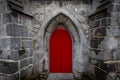 Scary pointy red wooden door in an old and wet stone wall building with cross, skull and bones at both sides. Concept mystery, Royalty Free Stock Photo