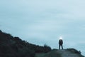 A scary silhouetted figure standing on the top of a path on a hill in the countryside, with a light glowing from his head. On a wi