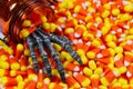 Scary skeleton hand coming out jar into a pile of candy corn