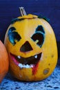 Scary smiling carved halloween jack o lantern with blood like painting on jaw and traces of blight around the eyes