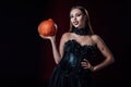 Vampire girl with fangs in black gothic dress holding Halloween pumpkin on black background Royalty Free Stock Photo