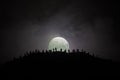 Scary view crowd of zombies on hill with spooky cloudy sky with fog and rising full moon. Silhouette group of zombie walking under