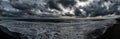 Scary weather sunset panoramic on the beach with dramatic sky with dark cumulus clouds and stormy sea with waves breaking on the Royalty Free Stock Photo