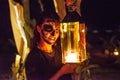 Scary woman witch with lantern and face pant during Halloween party at the artificial cemetery on the beach