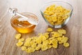 Scattered corn flakes, honey dipper on bowl with honey, bowl with cornflakes on table Royalty Free Stock Photo