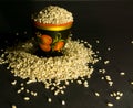 Scattered grains of oatmeal with a painted wooden cup on a black background