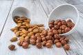 Scattered hazlenuts and almond seeds with white bowls on wood table Royalty Free Stock Photo